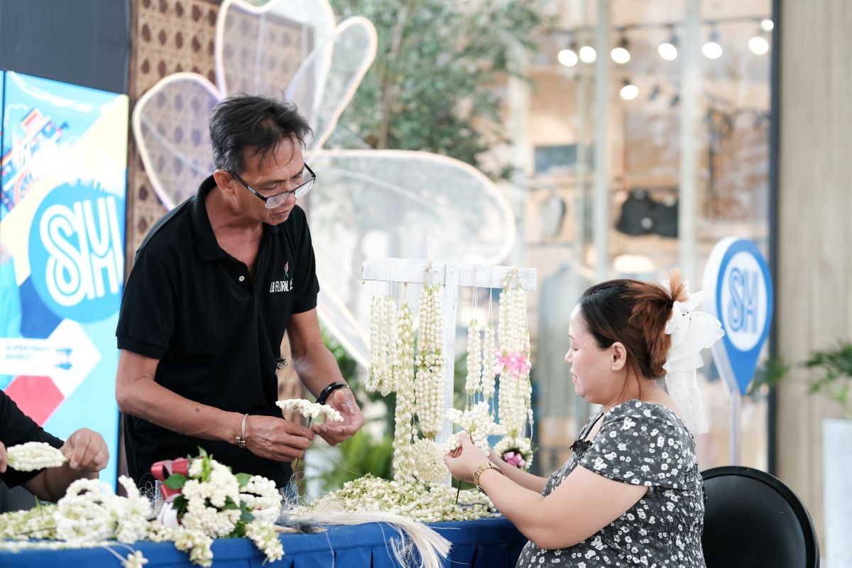 An_SM_shopper_receives_a_free_lesson_from_a_San_Pedro_Sampaguita_maker_on_how_to_make_garlands_and_lies